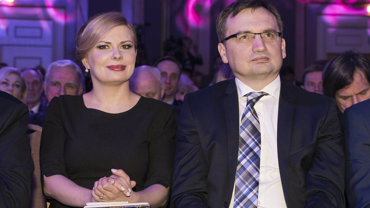 Mężczyzna w okularach w garniturze i kobieta w czarnej sukience siedzą obok siebie.