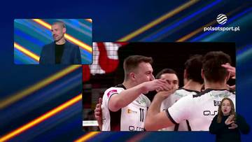 Dw&oacute;ch polskich siatkarzy w białych strojach sportowych, jeden z nich dotyka usta drugiego w geście przyjaźni lub gratulacji. W tle widać innych członk&oacute;w drużyny. Na mniejszym ekranie po lewej stronie widoczny jest mężczyzna w niebieskiej marynarce i czarnej koszulce.
