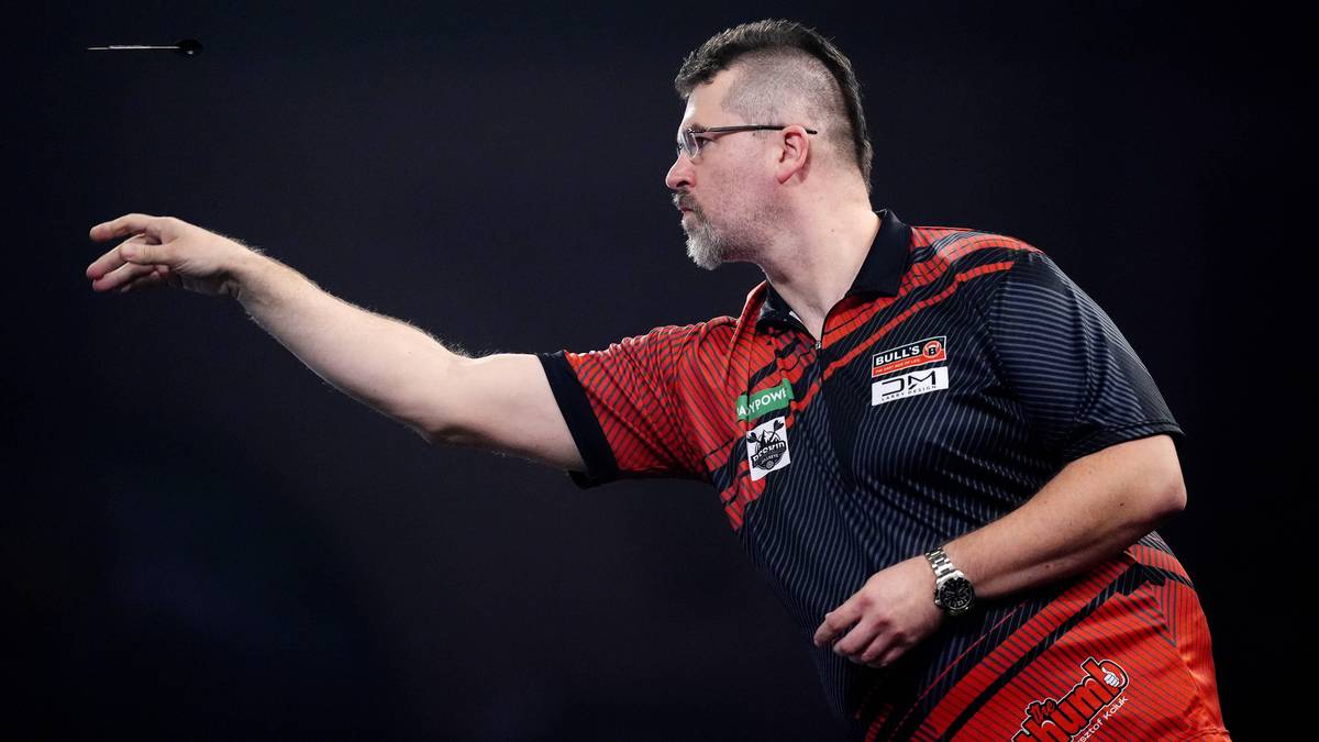 Darter Krzysztof Kciuk rzuca lotką w stronę tarczy.