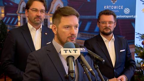 Maciej Biskupski przemawia do mikrofonu, obok niego stoją dwaj mężczyźni.