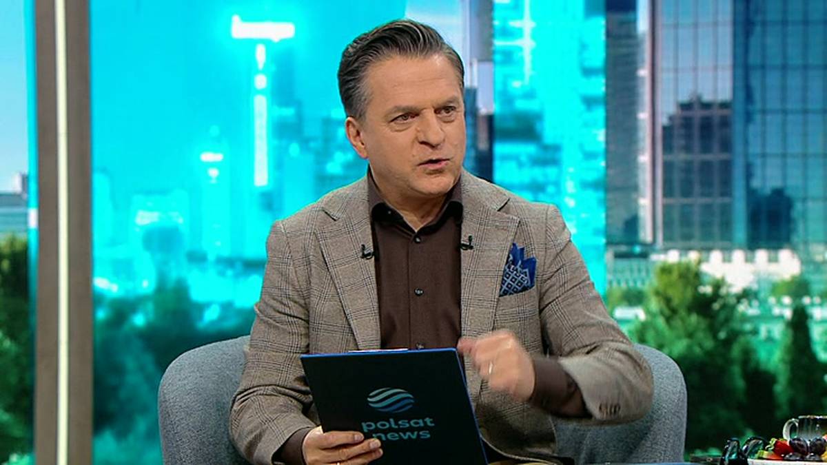 Mężczyzna w garniturze siedzi w fotelu i trzyma w rękach tablet z logo Polsat News.