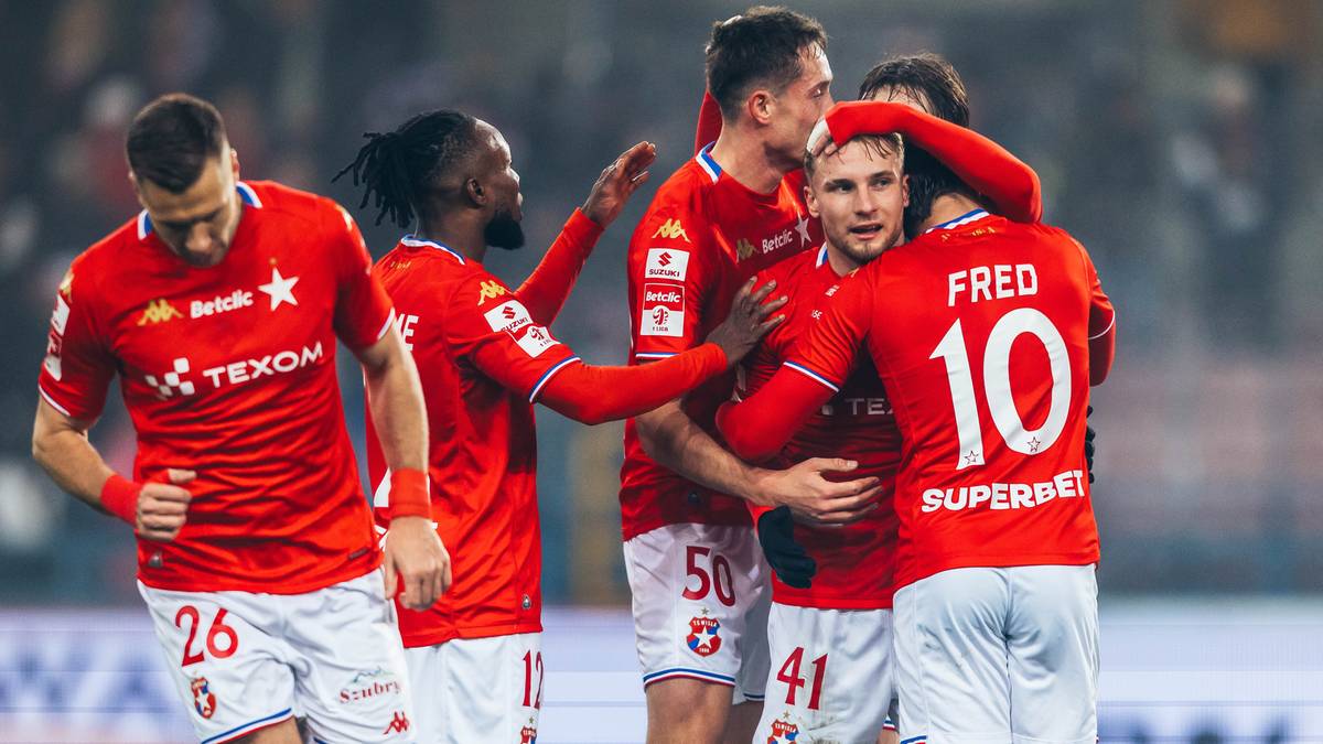 Piłkarze w czerwonych koszulkach celebrują zwycięstwo, obejmując się na boisku piłkarskim.