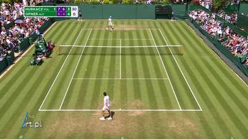 Kort tenisowy podczas meczu Wimbledonu z widokiem z g&oacute;ry na dw&oacute;ch graczy i trybuny pełne widz&oacute;w. Na ekranie widoczny jest wynik meczu.