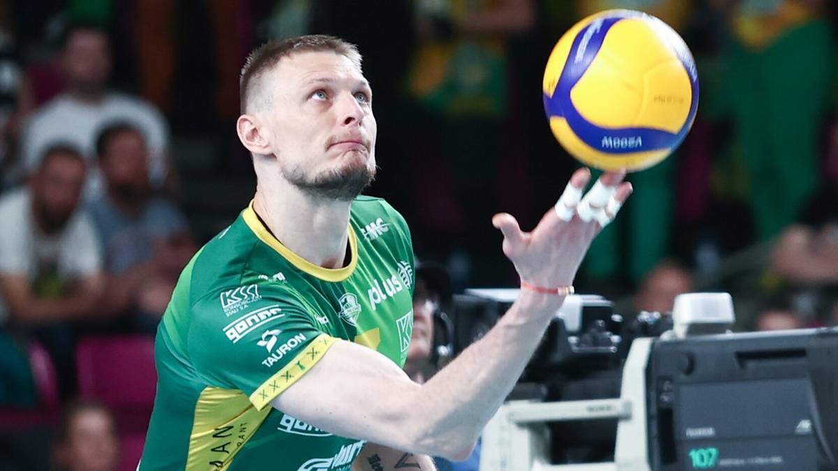 Siatkarz w zielono-żółtym stroju odbija piłkę nad głową.