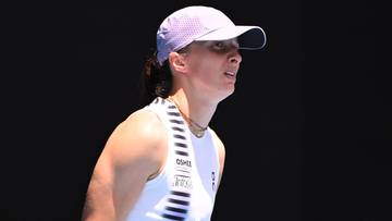 Iga Świątek w białej koszulce tenisowej i jasnor&oacute;żowej czapce z daszkiem, z profilu, z zamkniętymi oczami.