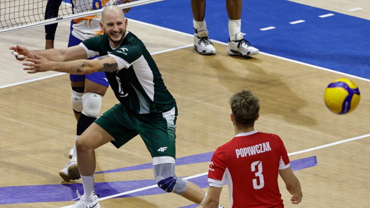 Gracz w zielonym stroju broni piłki do siatkówki podczas meczu.