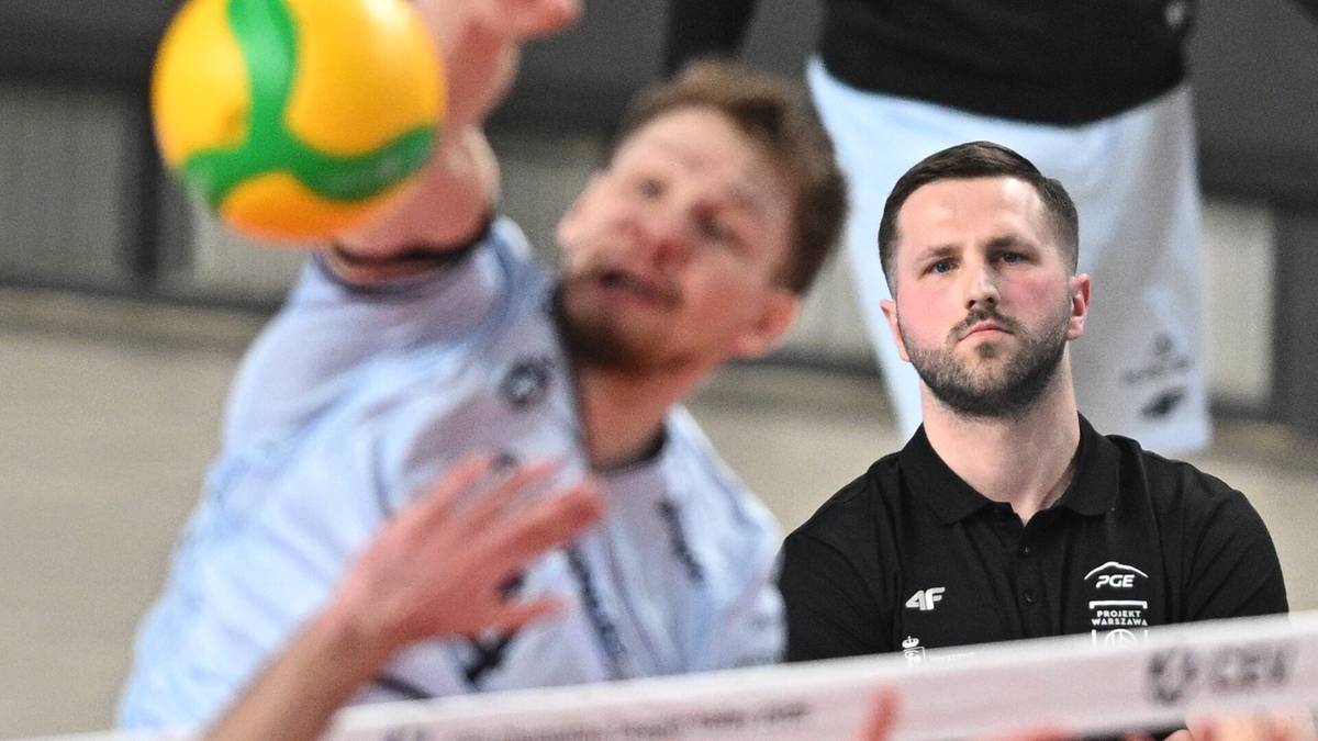 Siatkarz wykonujący zagrywkę, obok niego trener patrzący w stronę obiektywu.