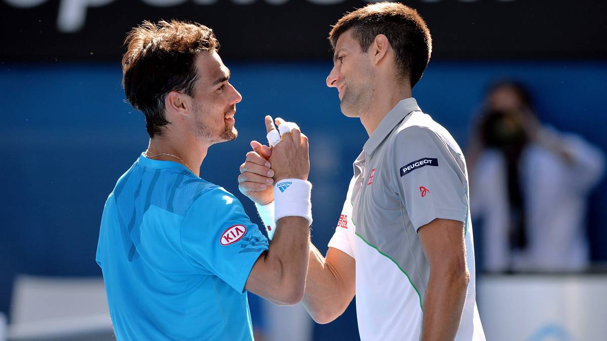 Dwóch tenisistów, jeden w niebieskiej koszulce z logo KIA, drugi w szarej koszulce, ściska sobie dłonie po meczu.