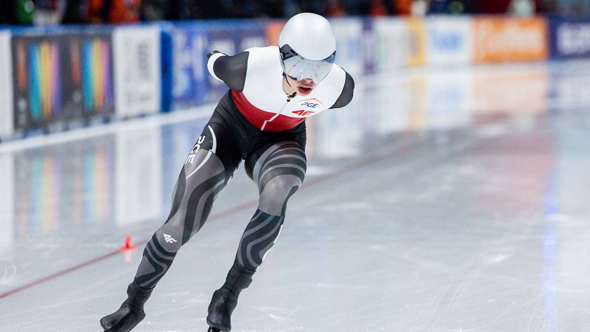 Panczenista w białym kasku i czarno-czerwonym stroju ślizga się po lodowisku podczas zawodów.