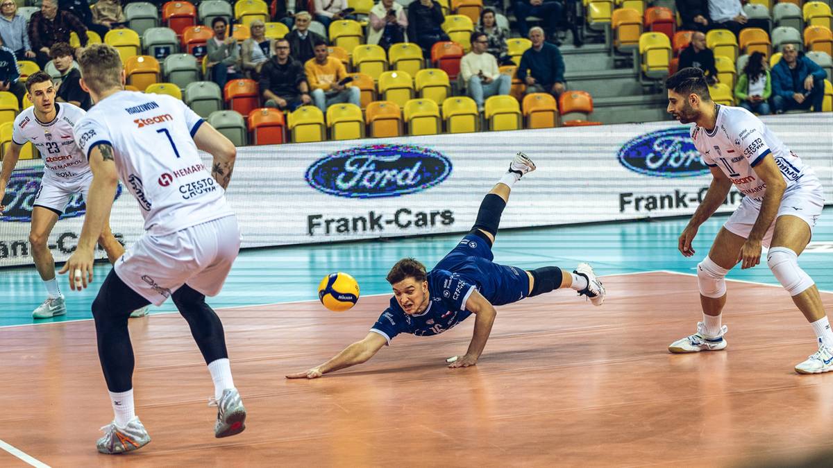 Siatkarz w ciemnym stroju wykonuje wślizg, próbując ratować piłkę podczas meczu.