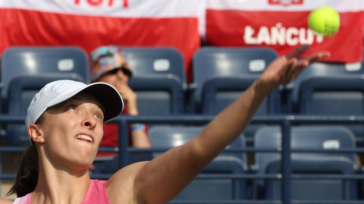 Tenisistka Iga Świątek podczas serwisu, z piłeczką unoszącą się w powietrzu nad jej dłonią.