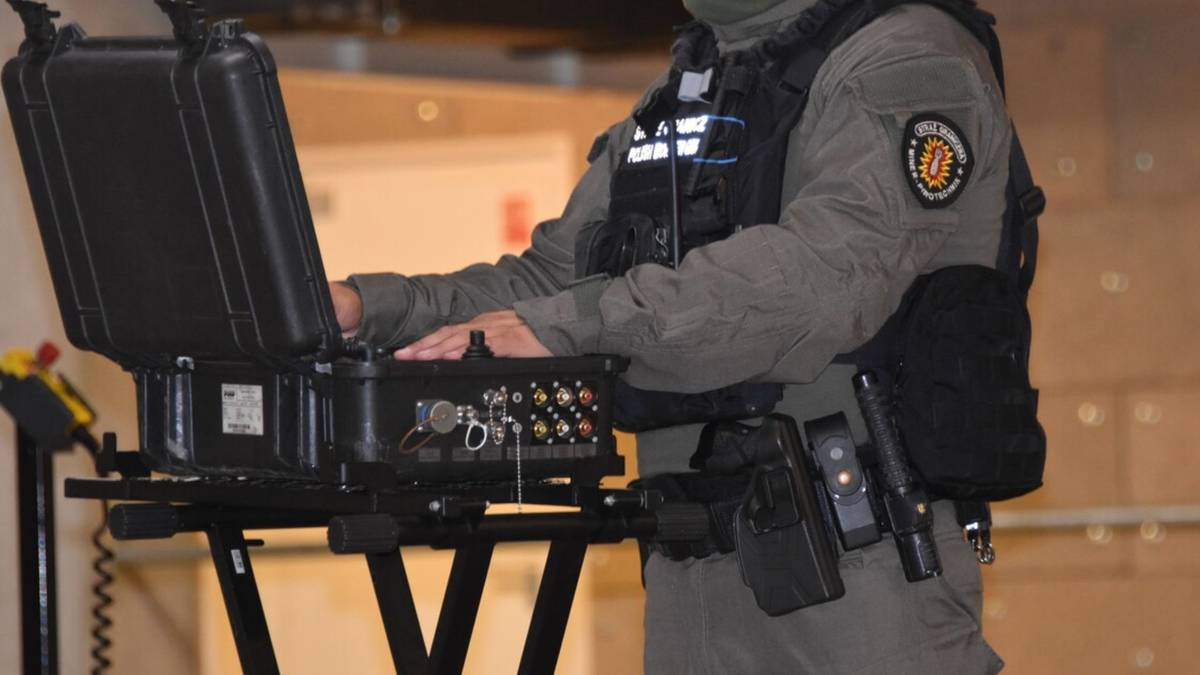 Funkcjonariusz Straży Granicznej w kamizelce taktycznej pracuje przy przenośnym urządzeniu technicznym w walizce.