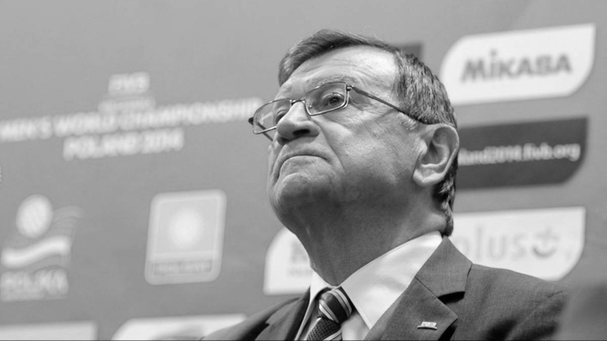 Mężczyzna w okularach i garniturze w tle z logotypami sportowymi.