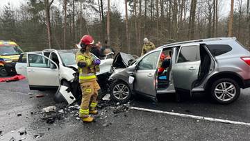 Strażak w odblaskowym stroju stoi przy wraku samochodu po czołowym zderzeniu dw&oacute;ch aut na drodze.