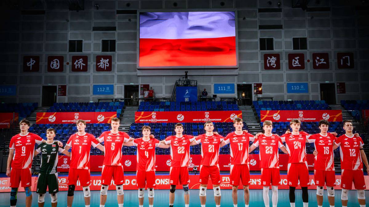 Reprezentacja Polski w siatkówce mężczyzn w czerwonych strojach stoi na boisku przed trybunami.