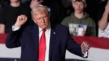 Donald Trump w garniturze i czerwonym krawacie, gestykuluje rękami podczas wystąpienia.