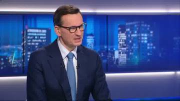 Mateusz Morawiecki w garniturze i krawacie, siedzący na tle nocnego miasta.