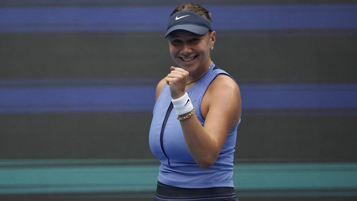 Portret tenisistki Amandy Anisimovej w niebieskiej koszulce sportowej, z zaciśniętą prawą pięścią uniesioną w geście triumfu. Uśmiechnięta, patrzy w bok.