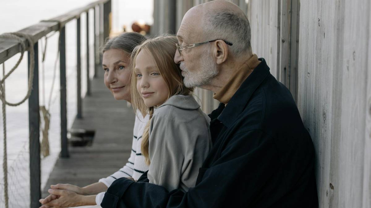 Trzy osoby siedzą obok siebie, starszy mężczyzna, młoda dziewczyna i starsza kobieta.
