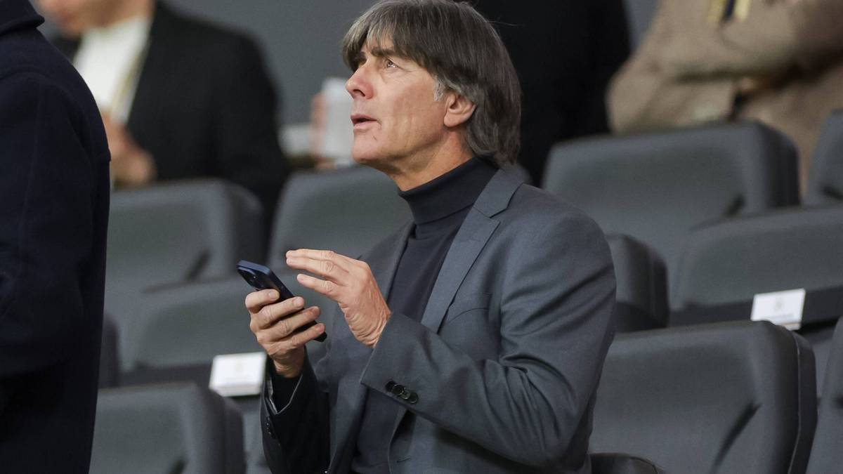 Joachim L&ouml;w siedzi na trybunach, patrząc w bok i trzymając telefon kom&oacute;rkowy w dłoniach.