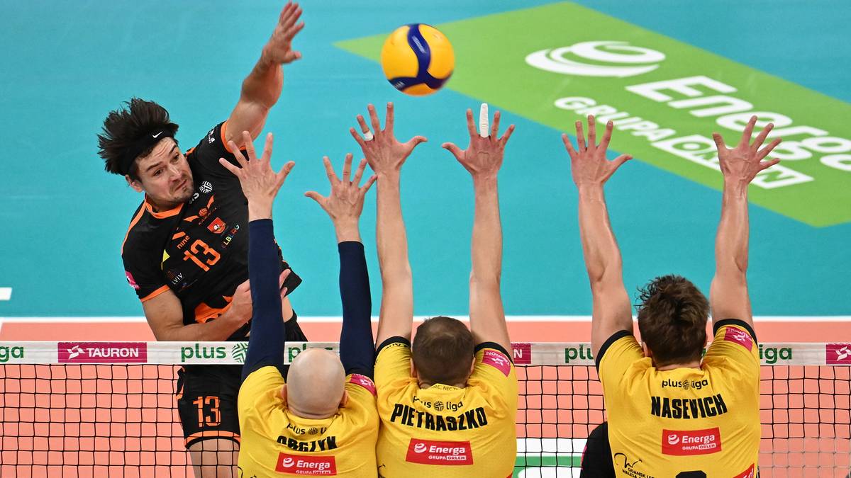 Siatkarz w czarnej koszulce z numerem 13 atakuje piłkę, podczas gdy czterech graczy drużyny przeciwnej w żółtych koszulkach próbuje ją zablokować.