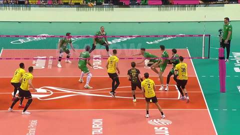 Mecz siatk&oacute;wki: zawodnicy w ż&oacute;łtych i zielonych strojach rywalizują na boisku, jeden z graczy w ż&oacute;łtym wykonuje atak.