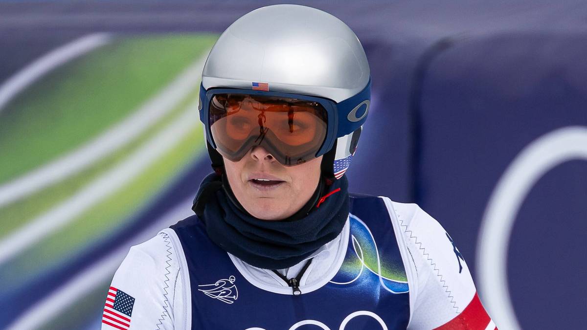Narciarka Lindsey Vonn w stroju sportowym z logo USA i kaskiem na głowie, trzymająca kije narciarskie.