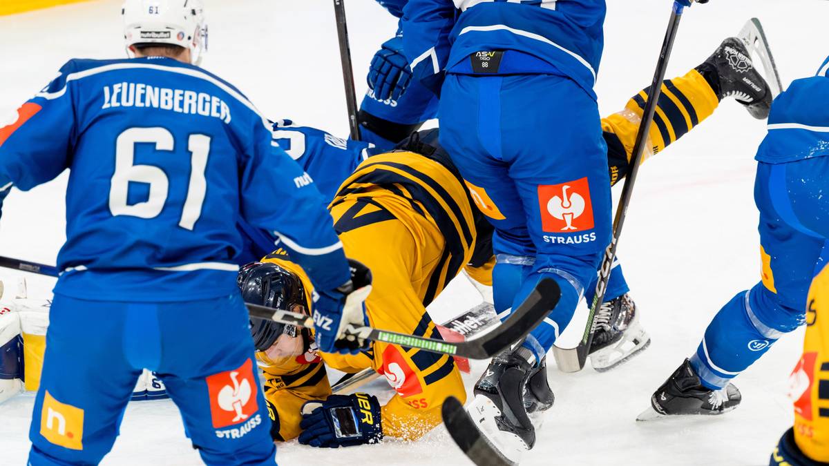 Hokeiści walczą o krążek na lodowisku, jeden z zawodników leży na lodzie.