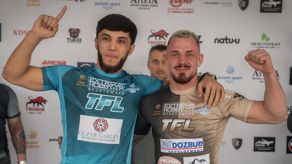 Dwóch mężczyzn w strojach sportowych stoi przed ścianką sponsorów, pozując do zdjęcia.