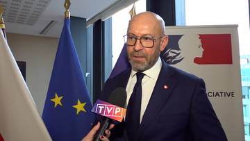 Jakub Rutnicki, ubrany w garnitur, udziela wywiadu przed flagą Unii Europejskiej i flagą Francji.