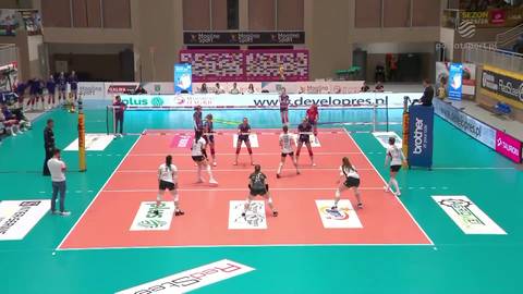 Boisko do siatk&oacute;wki z zawodniczkami obu drużyn, gotowymi do akcji, oraz widoczną publicznością.