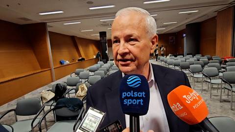 Apoloniusz Tajner, starszy mężczyzna w garniturze, udziela wywiadu przed mikrofonami Polsat Sport i "Jedyneki". W tle widoczne są rzędy pustych krzeseł na sali konferencyjnej.