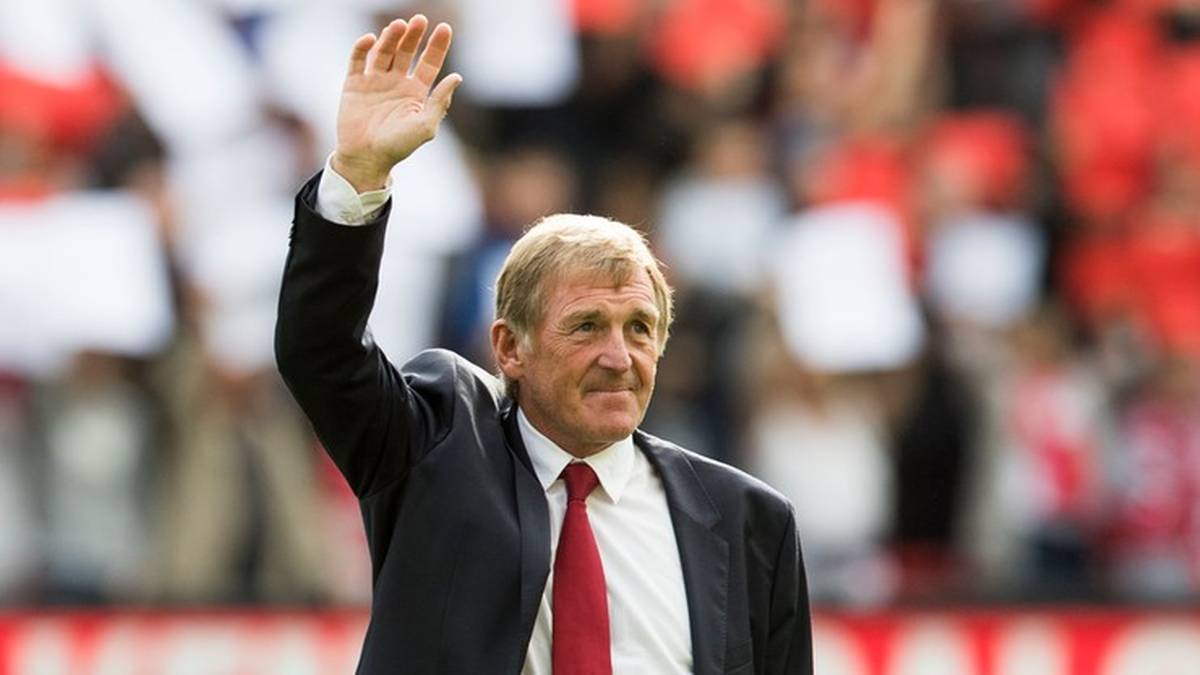 Kenny Dalglish w garniturze i czerwonym krawacie macha do publiczności.