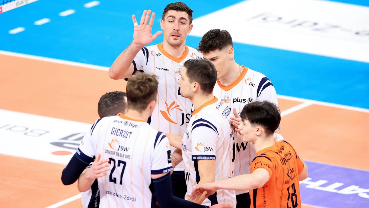 Grupa siatkarzy Jastrzębskiego Węgla w dyskusji na boisku, jeden z zawodników podnosi rękę.