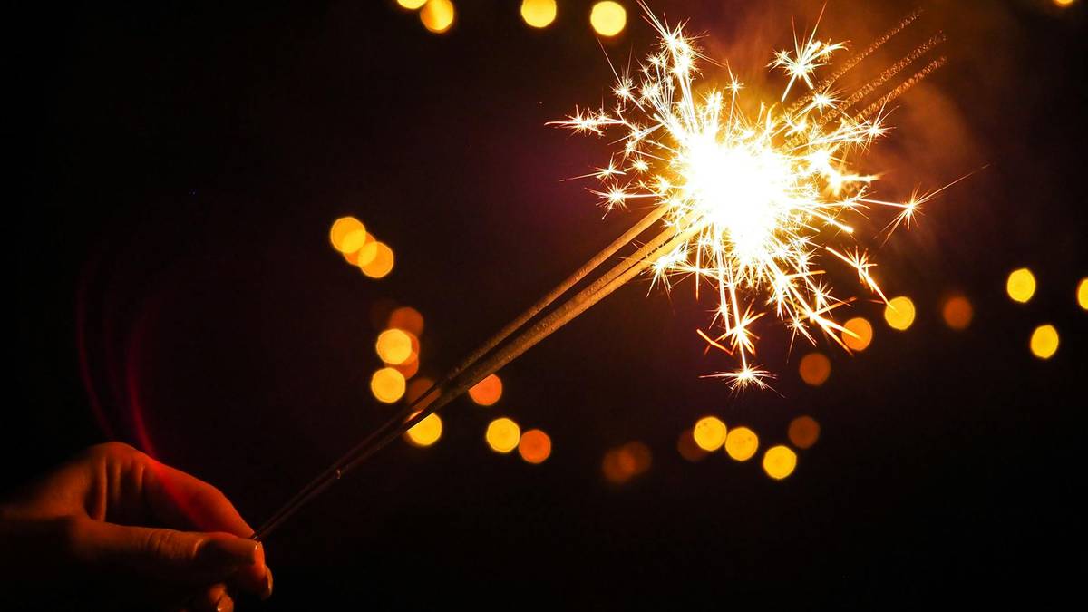 Ręka trzymająca płonącą zimną ognia na ciemnym tle z rozmazanymi, ciepłymi światłami.