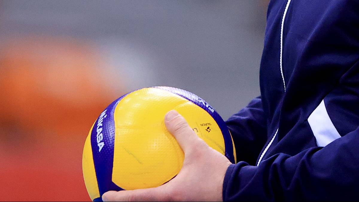 Trener siatk&oacute;wki z piłką w dłoni, skupiony na grze.