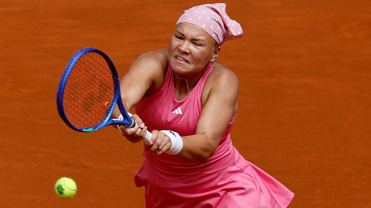 Tenisistka w r&oacute;żowej sukience i opasce na głowie uderza rakietą tenisową piłkę na korcie ziemnym.