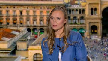 Katarzyna Niedźwiedzka, kobieta z blond włosami w niebieskiej marynarce, patrzy w bok, siedząc na tle nocnego miasta.