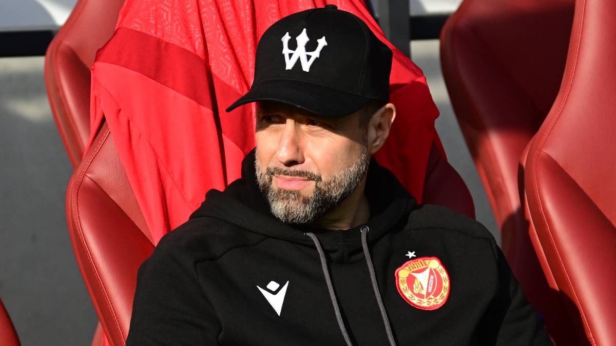 Mężczyzna w czapce i bluzie sportowej siedzi na ławce rezerwowych.