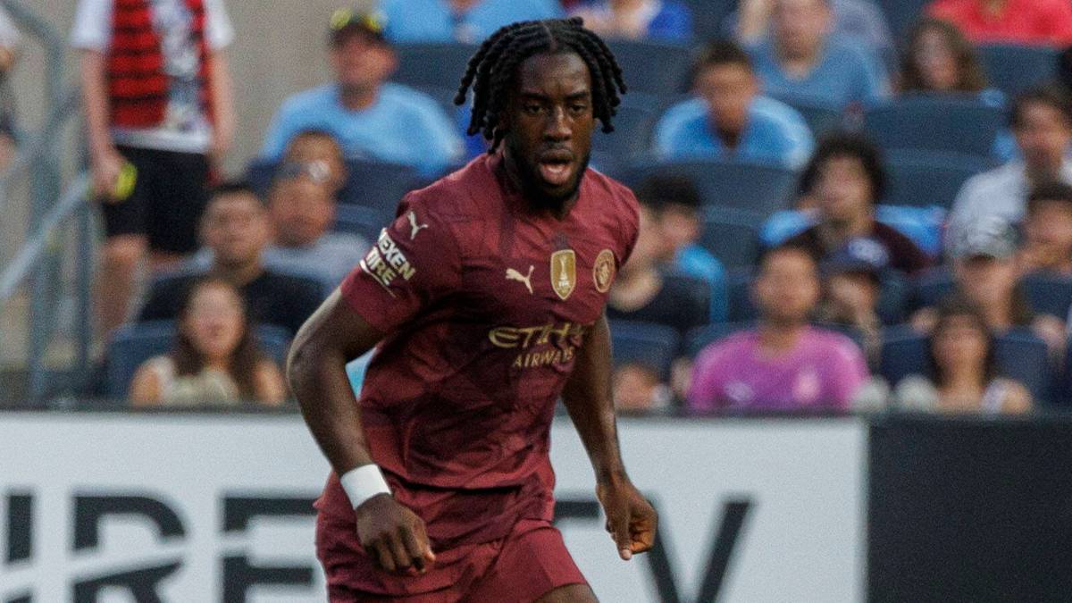 Piłkarz w bordowej koszulce z krótkim rękawem i spodenkami, grający w meczu piłki nożnej, z białym zegarkiem na lewym nadgarstku. W tle widzimy trybuny stadionu wypełnione publicznością.