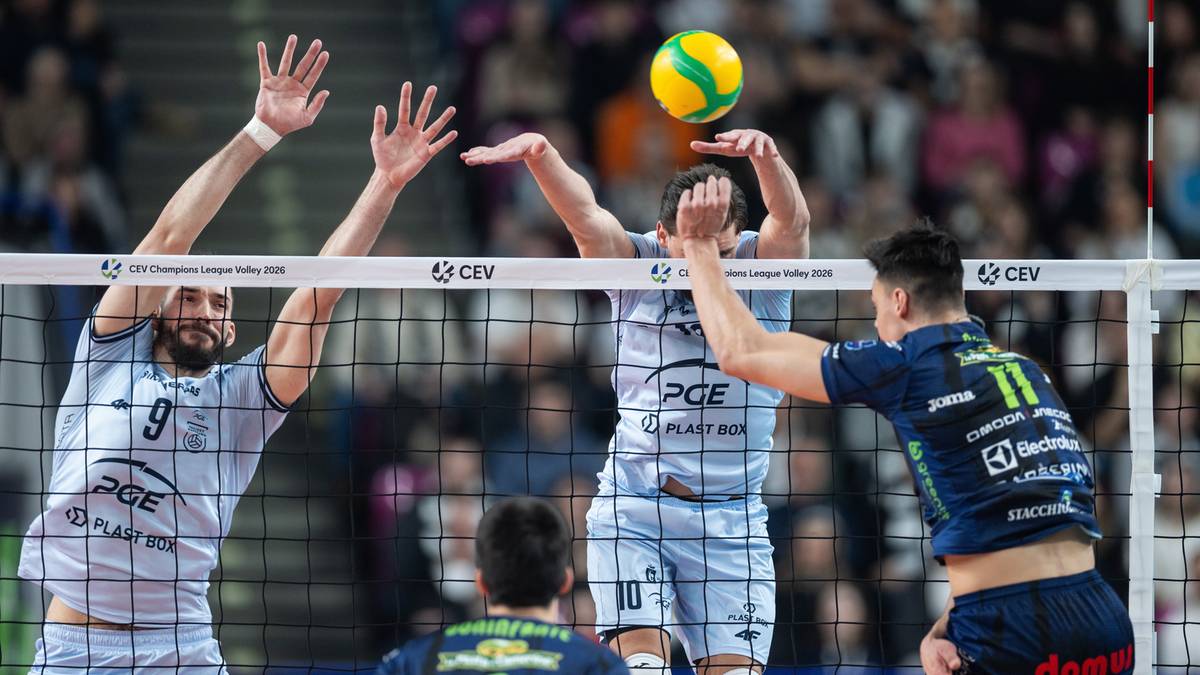 Siatkarze blokują atak podczas meczu siatk&oacute;wki, w tle widownia.