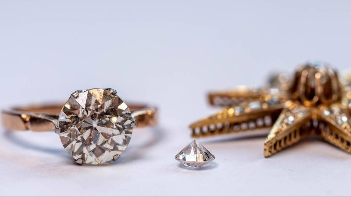 Złoty pierścionek z dużym brylantem, pojedynczy brylant i ozdobna złota zawieszka wysadzana kamieniami na jasnym tle.