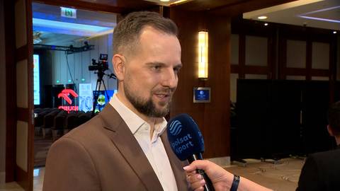 Mężczyzna w garniturze udziela wywiadu z mikrofonem, w tle sala konferencyjna.