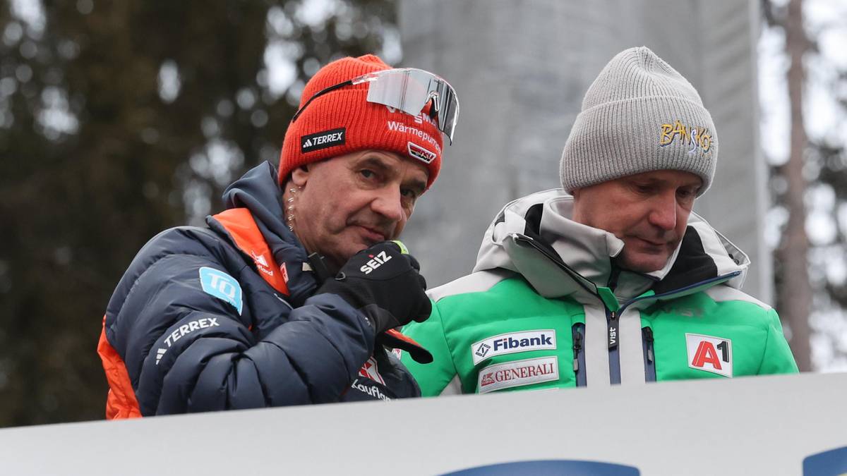 Dw&oacute;ch mężczyzn w zimowych czapkach i kurtkach, prawdopodobnie trener&oacute;w skok&oacute;w narciarskich, stojących obok siebie podczas zawod&oacute;w.