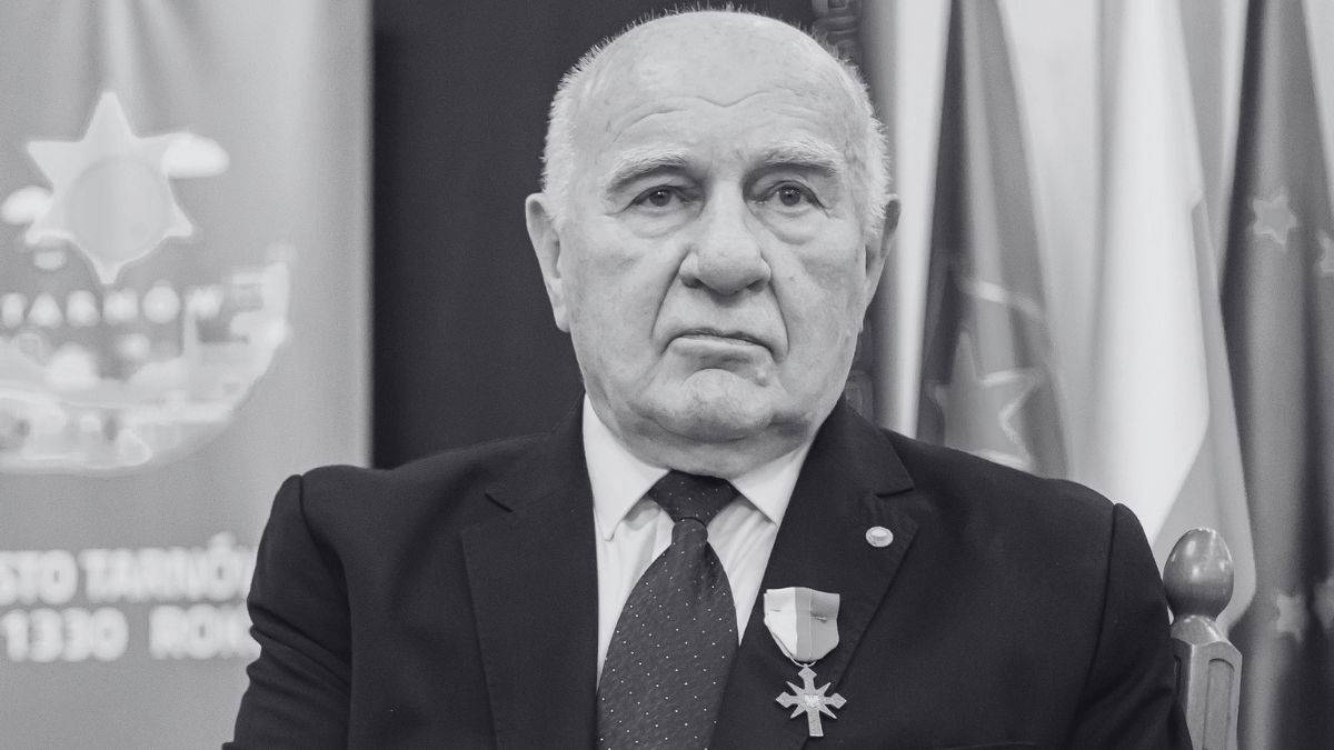 Portret Stanisława Majorka w garniturze, z widocznym medalem na piersi, na tle flag.