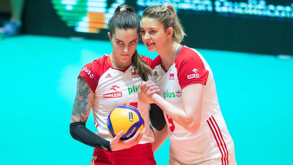 Dwie siatkarki w czerwono-białych strojach sportowych stoją obok siebie, jedna z nich trzyma piłkę do siatk&oacute;wki.