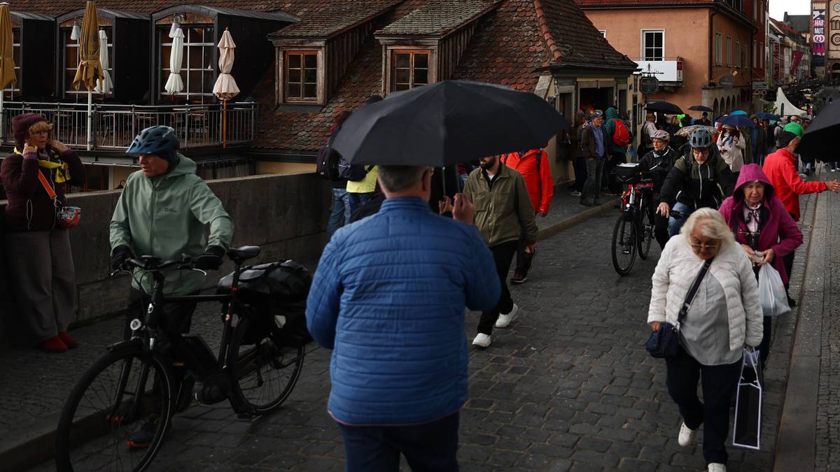 Grupa os&oacute;b idąca ulicą pod parasolami w deszczowy dzień, z widoczną starą zabudową miejską w tle.
