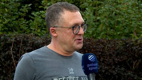 Mężczyzna w okularach trzymający mikrofon Polsat Sport.