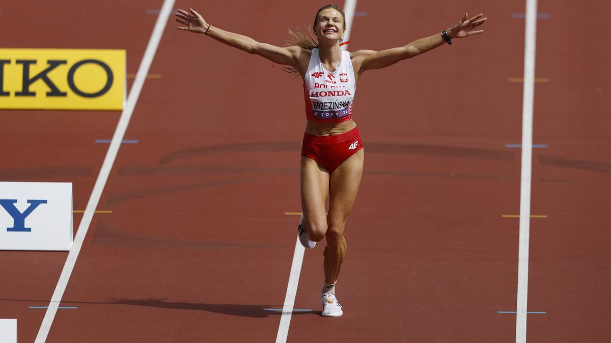 Uśmiechnięta sportsmenka w biało-czerwonym stroju sportowym, z rękami uniesionymi do góry, przekracza linię mety biegu.