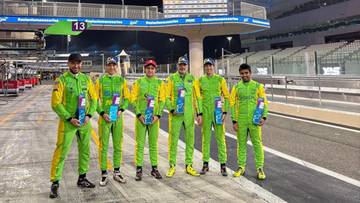 Grupa mężczyzn w zielonych kombinezonach wyścigowych stoi w szeregu, trzymając w rękach przedmioty przypominające butelki.